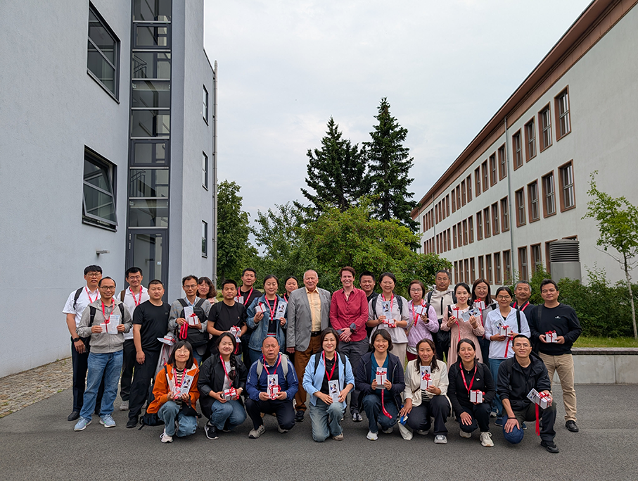 Eine Gruppe von 33 chinesischen Berufsschullehrern steht gemeinsam mit Vertreterinnen und Vertretern der Staatlichen Studienakademie Riesa einem Gebäude der Staatlichen Studienakademie Riesa. Im Hintergrund ist das Gebäude zu sehen. Die Delegation ist im Rahmen eines Weiterbildungsprogramms der TU Dresden zu Gast und informiert sich über das duale Studium in Deutschland