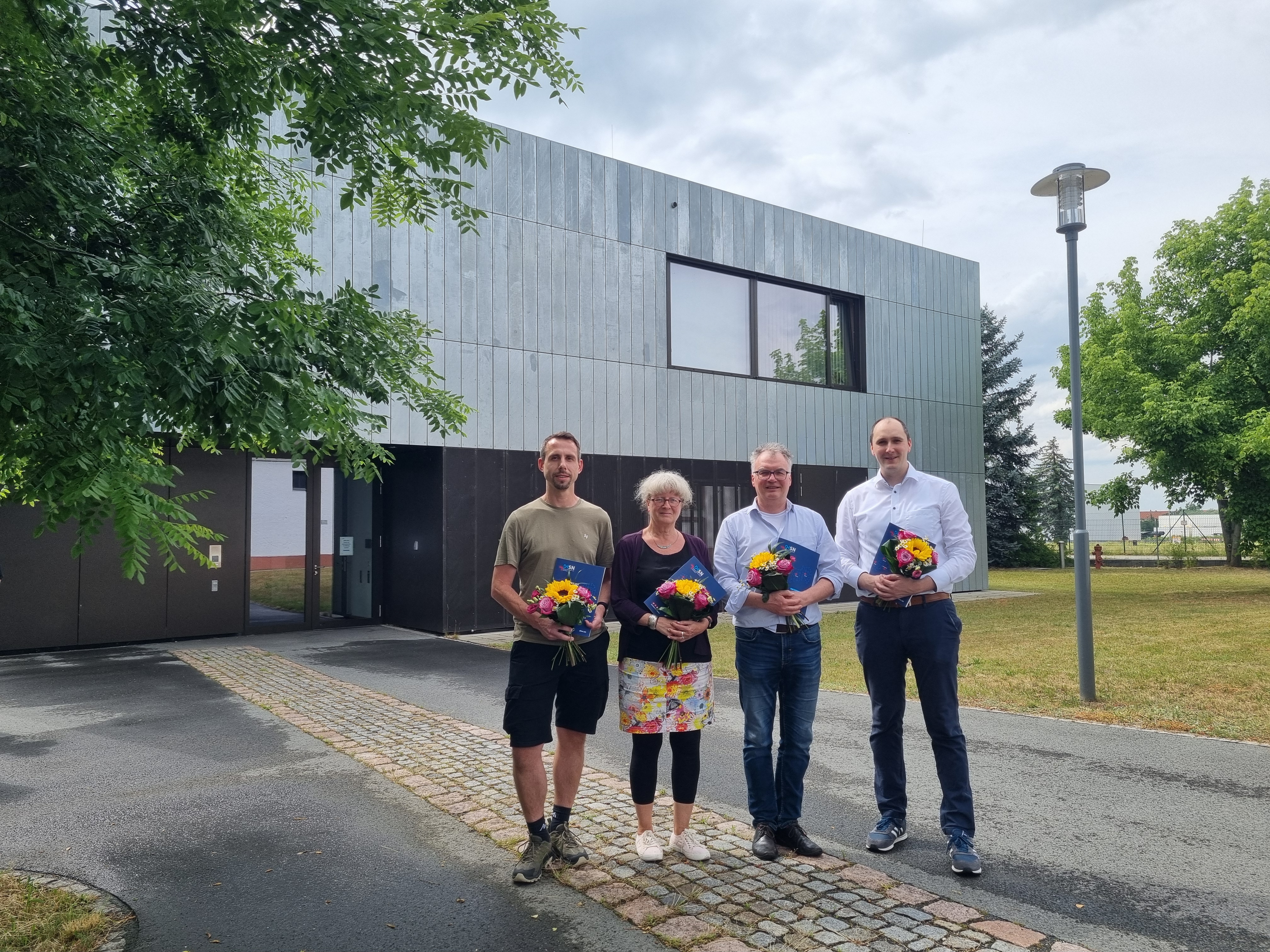 Die vier gewählten Studienleiter werden mit einem Strauß Blumen vor dem Haus 6 fotografiert